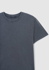 T-shirt in cotone grigio scuro con collo rotondo, maniche corte e una texture morbida. Presenta un'etichetta con la scritta "CALLIOPE" all'interno del collo.
