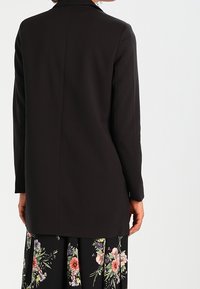 Black long-sleeve blazer with a tailored fit, featuring a notch collar and a smooth texture, worn over a floral-patterned skirt.