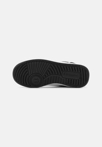 Semelle de sneaker en caoutchouc noir avec un motif texturé et une marque prédominante. Dispose d'un talon courbé et d'un relief de traction pour une meilleure adhérence.