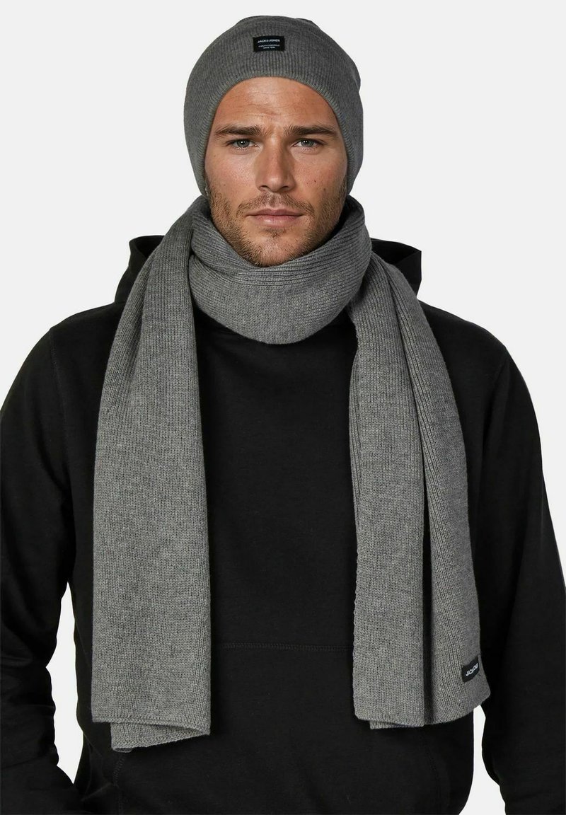 Gray ribbed knit beanie and matching scarf, both made of soft material, draped around the neck, worn over a black hoodie.