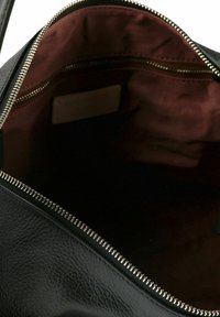 Schwarze Ledertasche geöffnet, die dunkelbraunes Stofffutter mit Metallreißverschlusstasche und silbernem Reißverschlussverschluss zeigt.