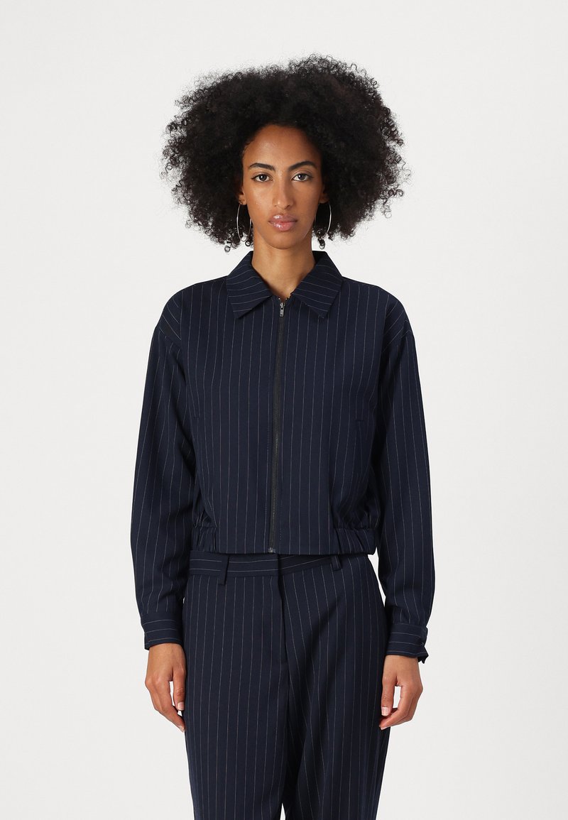 Marineblauwe pinstripe blazer met een cropped ontwerp, ritsopening en kraag. Gemaakt van een gladde stof met lange mouwen en details van elastische zoom.