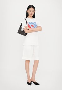 Hvit t-skjorte med blå og rød grafikk, kombinert med hvite plisserte shorts og svart posete håndveske. Sorte mules fullfører antrekket.
