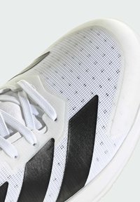 Białe buty sportowe z siateczkową cholewką i czarnymi akcentami, z trzema paskami, teksturowaną powierzchnią i okrągłymi sznurówkami. Podeszwa jest biała i solidna.