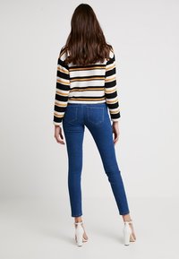 Suéter de punto acanalado a rayas en negro, blanco y amarillo, combinado con jeans de mezclilla ajustados en azul. Sandalias de tacón blanco visibles.