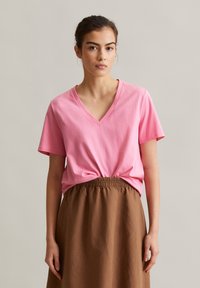 Rosa Baumwoll-V-Ausschnitt-T-Shirt mit kurzen Ärmeln, kombiniert mit einem braunen Rock mit elastischem Bund. Einfaches Design und angenehme Textur.