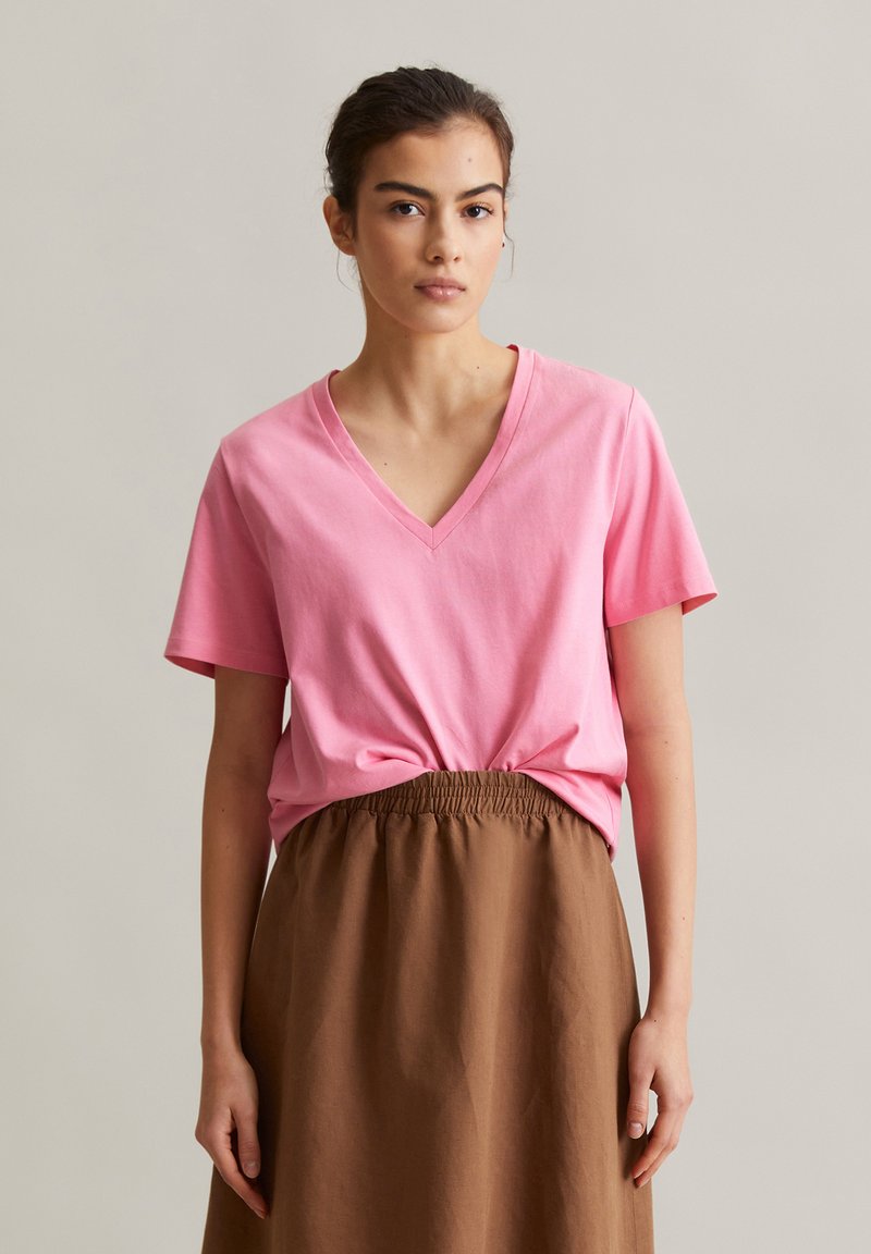 Rosa Baumwoll-V-Ausschnitt-T-Shirt mit kurzen Ärmeln, kombiniert mit einem braunen Rock mit elastischem Bund. Einfaches Design und angenehme Textur.