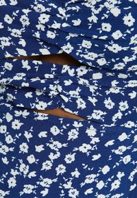 Blue floral patterned dress with white flowers, featuring gathered fabric design, cutouts, and textured fabric for added visual interest.