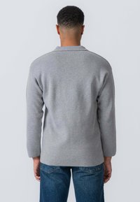 Grå strikket sweater med en afslappet pasform, lange ærmer og en let buet kant. Bæres med blå denimjeans, der viser et afslappet look.