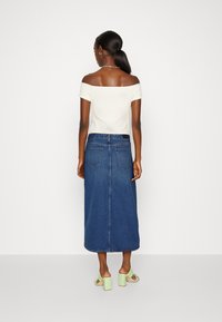 Haut blanc à fines côtes dénudé des épaules associé à une longue jupe en denim. La jupe présente une coupe décontractée et des poches arrière, vue de dos.