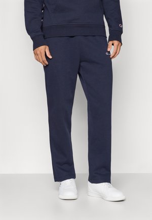 Mørkeblå sweatpants lavet af blødt stof, med en afslappet pasform og elastisk talje. Båret med hvide sneakers.