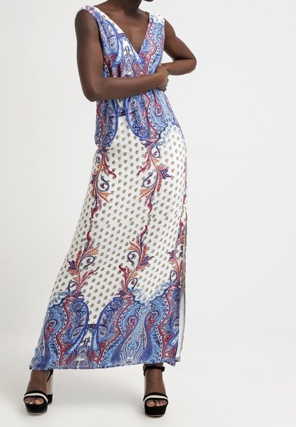 Robe maxi avec décolleté en V, motif cachemire bleu et rouge sur fond blanc, dotée de fentes latérales et d'un tissu léger. Sandales à talons noires.