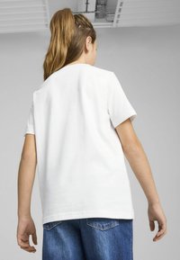 Camiseta de algodón blanca con mangas cortas y un ajuste relajado, vista desde la espalda, combinada con pantalones cortos de mezclilla azules. Textura suave.