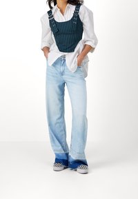 Saviininvihreä, ohuin raidoin kuvioitu lyhyt toppi hihnoilla, käytetty valkoisen nappipaidan päällä, yhdistetty vaaleansinisiin leveälahkeisiin farkkuihin ja ruutukuviollisiin tennareihin.