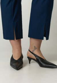 Zwarte leren slingback hakken met puntige neuzen en een kleine kittenhak; gecombineerd met marineblauwe cropped broeken met zijslits.