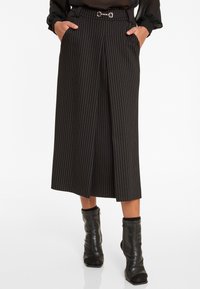 Schwarze, gestreifte Culottes mit einem Taillengürtel, seitlichen Taschen und einem dekorativen silbernen Akzent. Hergestellt aus glattem Stoff.