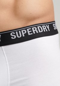 Ropa interior con cinturilla blanca que presenta una banda elástica negra con el logotipo "SUPERDRY". La textura suave y el diseño ajustado realzan la comodidad.