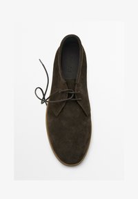 Chaussure en daim marron avec un bout arrondi, design classique à lacets, et une semelle en caoutchouc beige. La partie supérieure présente des coutures visibles et une texture lisse.