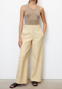 Top ajustado color beige combinado con pantalones de tiro alto y pernera ancha de color amarillo claro. Sandalias de tiras negras completan el conjunto. Textura de tela suave.