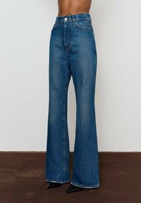 Džíny s vysokým pásom, rozšírené v spodnej časti, vyrobené z modrej denimovej látky, s dizajnom piatich vreciek a kontrastným prešívaním. Obsahujú uzáver na gombík a zips.