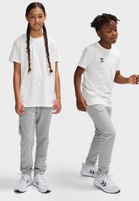 To børn modellerer afslappede outfits: en hvid T-shirt med et logo, grå sweatpants og hvide træningssko. Teksturopbevisning, afslappet pasform.