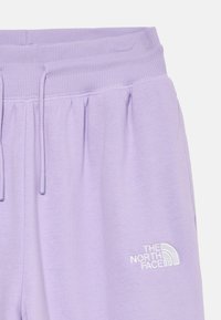 Lila trenirke z elastičnim rebrastim pasom, vrvico za zategovanje, stranskima žepoma in belim vezenim logotipom The North Face na desni nogi.