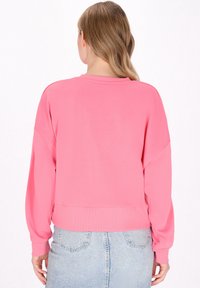 Felpa rosa corta con maniche lunghe, vestibilità comoda e polsini a coste. Tessuto dalla consistenza liscia, senza motivi o dettagli in metallo visibili.