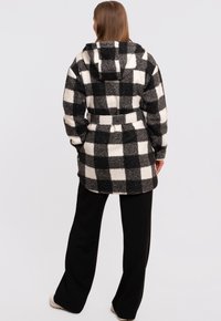 Kostkovaný fleecový kabát v černobílé barvě, s kapucí a páskem. Měkká textura, střední délka, velký čtvercový vzor.