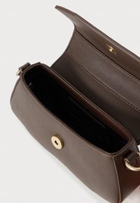 Geantă mică din piele taupe cu clapetă, închidere magnetică aurie, și interior din material textil negru, prezentată deschisă pe o suprafață albă.