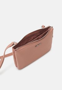 Borsa a tracolla in pelle rosa di Calvin Klein con una texture liscia, chiusura con zip e un design elegante. Gli interni presentano una fodera in tessuto abbinato.
