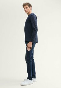 Laaja tummansininen pitkähihaisena paita yhdistettynä tummansinisiin farkkuihin ja valkoisiin tennareihin, esitetty sivulta. Silkkinen kangas, slim fit, yksinkertainen muotoilu.