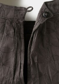 Tissu gris foncé avec broderie florale texturée, comportant un rabat boutonné et une petite boucle sur les bords supérieurs.