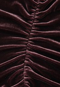 Tmavě sametová látka s výrazným řasením uprostřed, která vykazuje bohatou texturu a hlubokou barvu, čímž zvyšuje její vizuální hloubku.