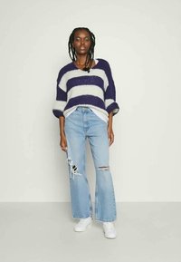 Sweater de malha com riscas roxas e brancas, corte solto, combinado com jeans claros de corte flare com detalhes desgastados. Ténis brancos.