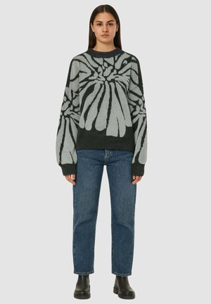 Maglione a maglia di colore verde scuro con un grande motivo floreale grigio, maniche lunghe e vestibilità ampia. Abbinato a jeans blu e stivali neri.