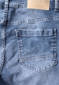 Jean en denim bleu clair avec une poche arrière dotée d'un bord cousu. Le tissu est lisse avec une texture délavée et une étiquette de marque en cuir au-dessus.