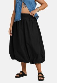 Svart, ballongstil kjol gjord av mjukt material med resårmidja. Parat med en denim crop top och svarta sandaler med nitar.