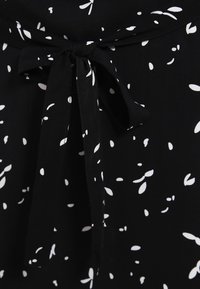 Tissu noir avec motif de feuilles blanches. Comprend un détail nœud papillon à la taille, mettant en valeur la douceur et le design du tissu.