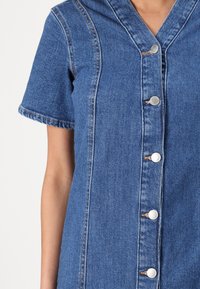 Denim-mekko lyhyillä hihoilla, v-kaula-aukolla, etunapeilla, vaaleansininen väri, kontrastiväritikkaukset ja hienovarainen rakenne.