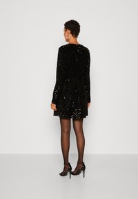 Svart paljettklänning med långa ärmar och rund halsringning. Tillsammans med svarta, remmade högklackade skor och genomskinliga svarta strumpbyxor.