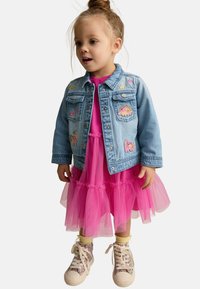 Jeansjacke mit buntem Tierstickerei, geschichtetes pinkes Tüllkleid, gelbe Leggings und gemusterte Sneaker mit Schnürsenkeln.