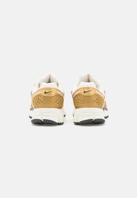 Nike-sneakers med ett överdel i vit mesh, guldaccent, texturerad häl och en svart gummisula. Har en synlig luftenhet och logotyp.