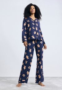 Marineblauw pyjama set met peperkoek en sterpatronen; lange mouwen, knoopsluiting bovenkant en wijde pijpen gemaakt van zacht stof.