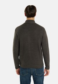 Grijze gebreide trui met een hoge kraag, geribde manchetten en zoom. Gemaakt met blauwe jeans, met een gladde textuur en een aansluitend ontwerp.