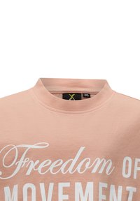Jasnoróżowa bawełniana koszulka z okrągłym dekoltem i dużym białym napisem "Wolność ruchu". Gładka tekstura, casualowy styl.