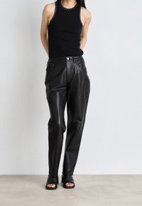 Žena v bezramínkovém černém topu s hřebíkovými okraji, černých kožených kalhotách s vysokým pasem a černých sandálech na podpatku s otevřenou špičkou.