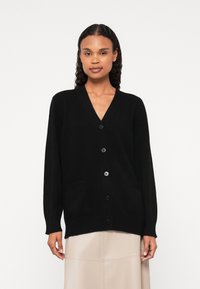 Cardigã preto feito de tecido suave, com decote em V, mangas longas, cinco botões e dois bolsos frontais. Textura lisa e ajuste relaxado.