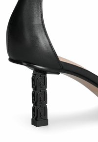 Sandal de tacón alto negro con parte superior de cuero suave y un tacón de bloque de patrón escultórico. El tacón tiene detalles en negro.