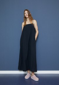 Černé, bezrukávové maxikabát s volným střihem a bočními kapsami; spárováno s růžovými, načechranými nazouvacími botami pro neformální vzhled.