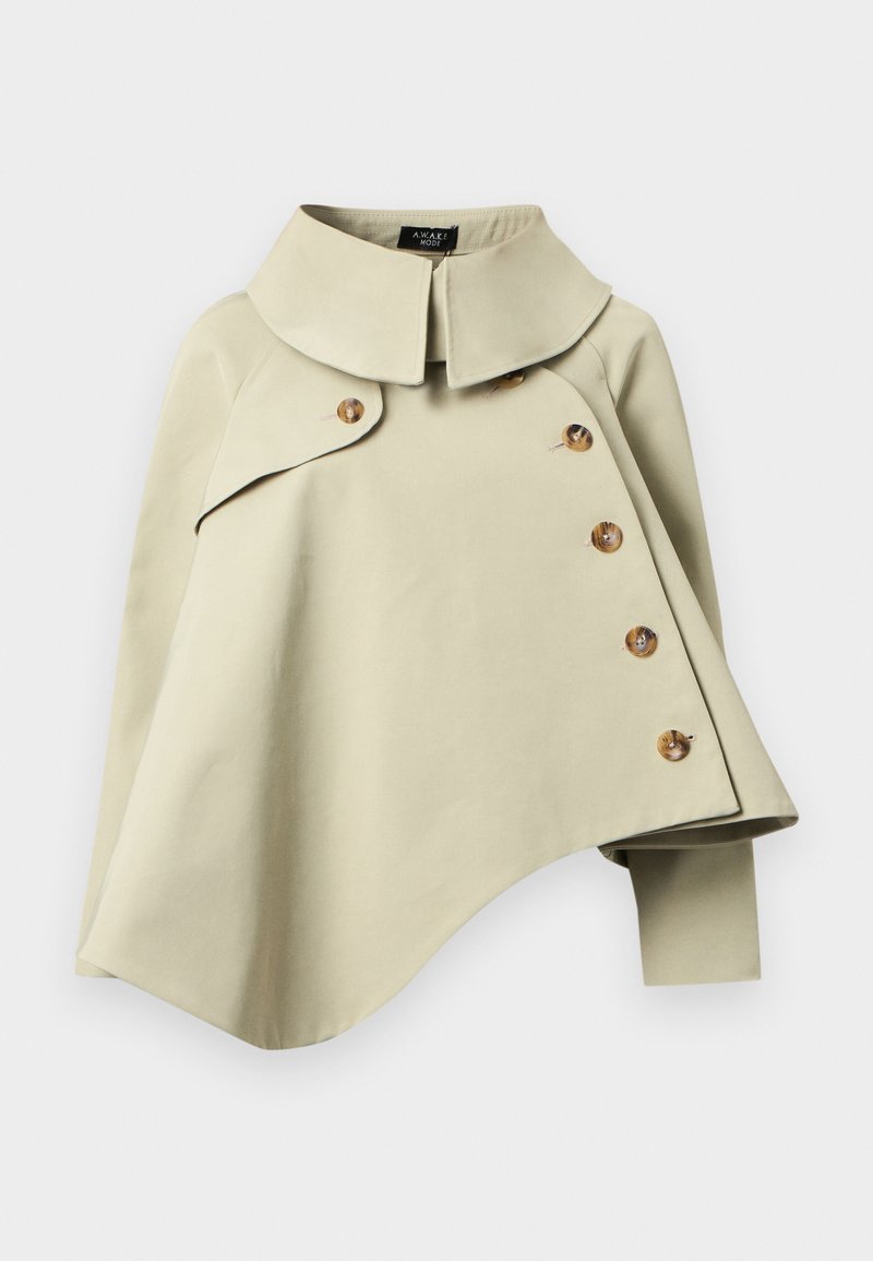 Veste cape cropped beige clair avec un large col, un ourlet asymétrique et cinq grands boutons marron. Tissu lisse, détails minimaux.